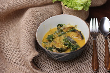 Catfish Curry with Cumin Leaves served in an art-patterned cup. On a brown wooden table.