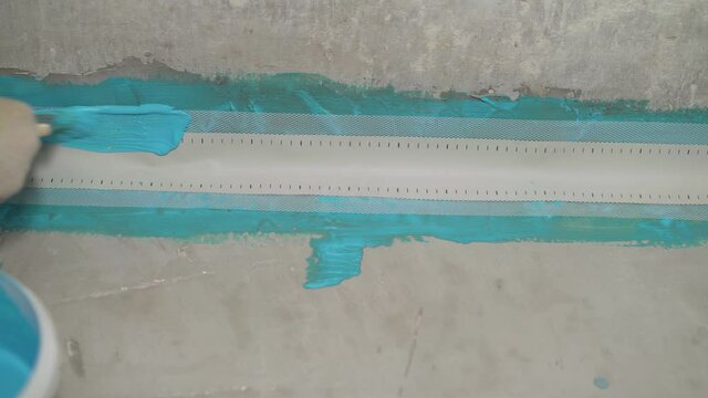 Close-up of a hand applying waterproofing in the bathroom. Worker is doing waterproof finish the bathroom floor in apartment is inder construction, remodeling, renovation, overhaul, extension, restora