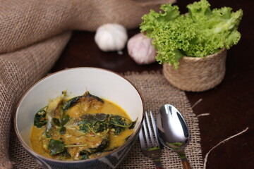 Catfish Curry with Cumin Leaves served in an art-patterned cup. On a brown wooden table.