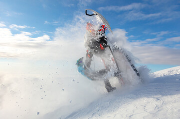 extreme driving of a mountain snowmobile. a sports snowmobiler in bright clothes and a helmet without brands, a colorful snowmobile of a new model. jumping with plumes and whirlwinds of snow