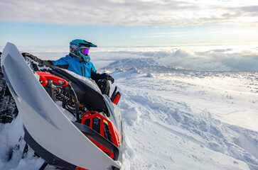 close-up of a powerful snowmobile piled on its side and a rider sitting on top of a mountain. a sports snowmobiler in bright clothes and a helmet without brands, a colorful snowmobile of a new model