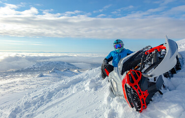 close-up of a powerful snowmobile piled on its side and a rider sitting on top of a mountain. a sports snowmobiler in bright clothes and a helmet without brands, a colorful snowmobile of a new model