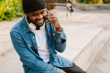 Black man with headphones talking on mobile phone while sitting on bench