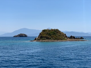Naklejka premium An uninhabited island in the Mediterranean. Islands surrounded by the sea, a quiet harbor for yachts. Seashore against the backdrop of mountains and clear sea.