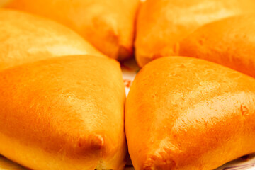 Homemade baked triangular buns lie on a plate, close-up.