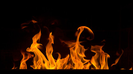 Fototapeta premium Bright orange bonfire flame on a black background. Abstract fiery texture. Realistic flame of fire burns the motion frame. Texture for design. The texture of fire. A blazing burning bonfire.