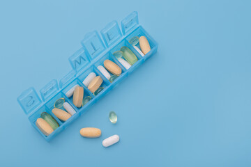 Organizer for pills, vitamins and dietary supplements on a light blue background. Health maintenance concept