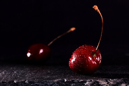 Sweet fresh red cherries on black stone background. Black background with space for text. Drops of water on the berries.