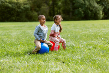 childhood, leisure and people concept - happy children bouncing on hoppers or bouncy balls at park