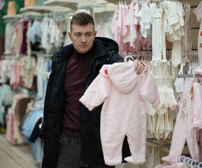 Photo of a handsome brunet young man who chooses baby clothes in a store in a mall. Shopping concept