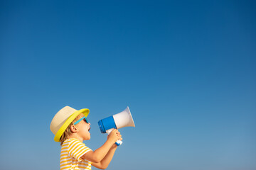 Happy child shouting through loudspeaker outdoor against blue sk