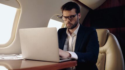 Businessman using blurred laptop near papers in private jet.