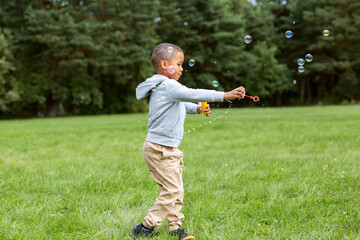 Fototapeta premium childhood, leisure and people concept - happy children blowing soap bubbles and playing at park