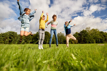 childhood, leisure and people concept - group of happy kids playing and jumping at park