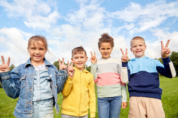 childhood, leisure and people concept - group of happy kids showing peace sign at park