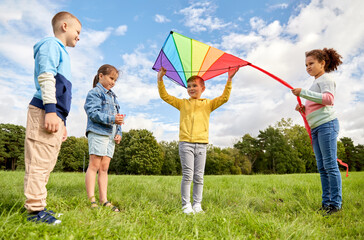 childhood, leisure and people concept - group of happy kids with kite playing at park