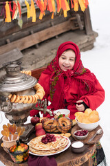 Shrovetide concept Maslenitsa. Joyful little girl sits at a table with a samovar and pancakes. Outdoor In Winter Time.