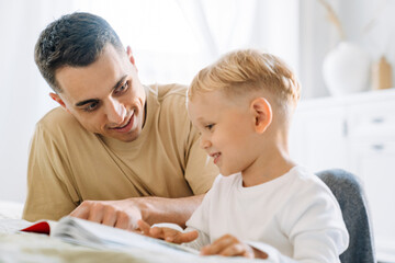 Obraz premium White father and his son reading book while spending time together