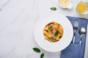 Bolognese Penne Pasta. Tasty appetizing classic italian penne pasta with parmesan cheese, basil and Bolognese sauce in white plate on plate on stone table Traditional dish of Italian cuisine. Top view