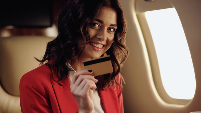 Cheerful businesswoman holding credit card in private plane.