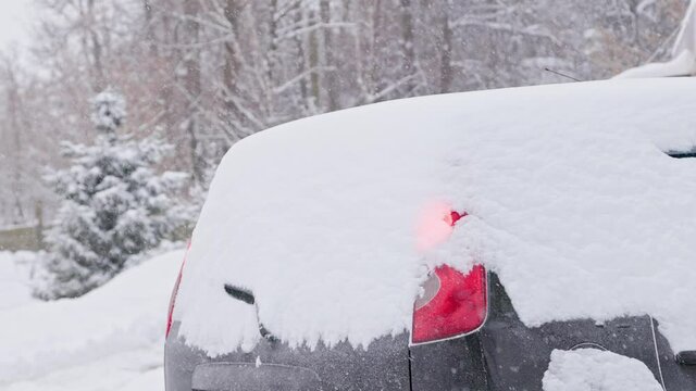 back side of snow covered black hatch back car at daylight snowfall, engine strated remotely