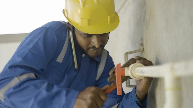 Plumber or repairman talking on mobile phone with colleague while fixing pipe using wrench - concept of communication, teamwork and technology