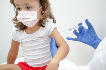 Criança sendo vacinada contra covid 19 volta as aulas medica com luva azul e seringa.
