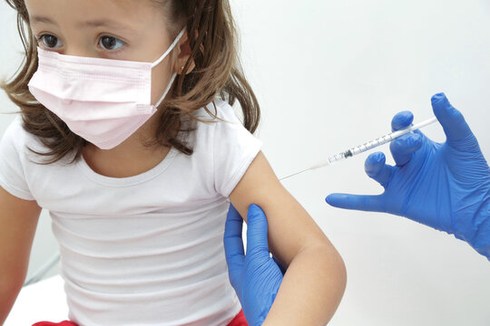 Crian&ccedil;a sendo vacinada contra covid 19 volta as aulas medica com luva azul e seringa.
