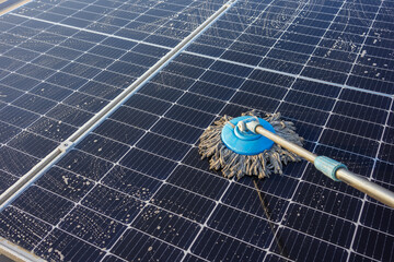 Man using a mop and water to clean the solar panels that are dirty with dust and birds' droppings...