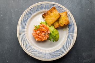 salmon Tartar on a plate with mashed avocado on grey concrete table top view