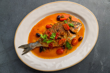 Dorado on grill in tomato sauce on a white plate on grey concrete table top view