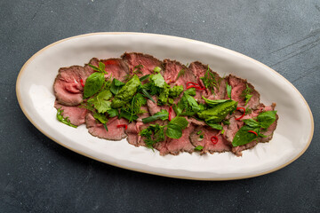 Sliced roast beef with greens and chili peppers on plate on grey concrete table top view