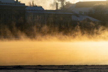 Steam comes out of the river in the city, soaring from the severe cold. Fog in frost winter weather at sunlight. 