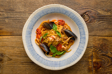 Pasta with seafood, shrimps, mussels and tomato sauce on old wooden table top view