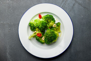 Broccoli in a white plate with garlic and sliced red pepper on grey concrete table top view