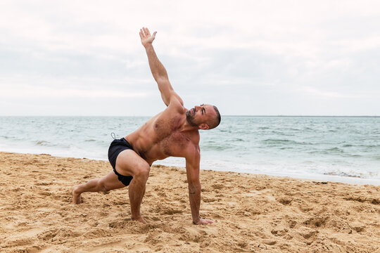 Shirtless man doing Side angle asana on beach