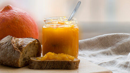 Pumpkin jam in a glass jar, bread with pumpkin jam, pumpkin on a wooden stand on a blurry...