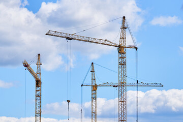 Industrial building cranes on background of cloudy sky. Hoisting cranes for creating multi-storey buildings of new city districts. Construction site background.