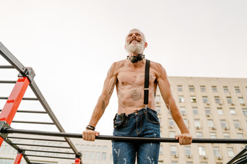 Adult white shirtless man doing workout using horizontal bar outdoors