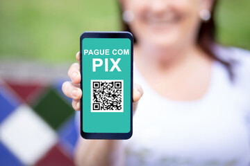 Woman holding a Smartphone and showing a QR Code on the screen to make payment through the PIX system.  PIX is a new electronic payment system in Brazil.