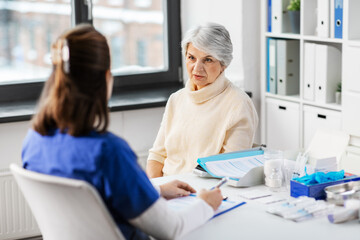 medicine, health and vaccination concept - doctor with clipboard and senior woman at hospital