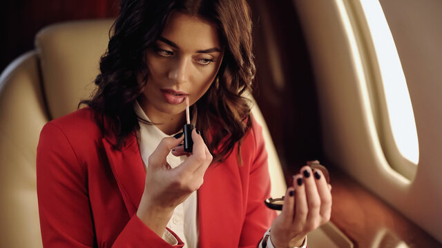 Businesswoman applying lip gloss and holding mirror in private jet.