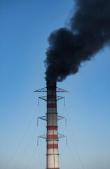 Large chimney of a thermal power plant with a stream of black smoke.