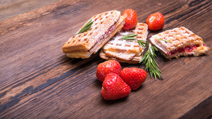 Wafers with marmalade and strawberries sprinkled with powder on an old wooden table, side view, copy space,