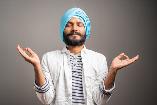 young indian sikh man relaxing by doing zen meditation on grey background - concept of relaxation, healthy lifestyle and leisure activities.