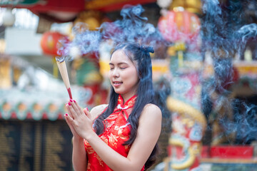 Asian woman in chinese dress traditional cheongsam holding incense pay homage to Chinese god at...