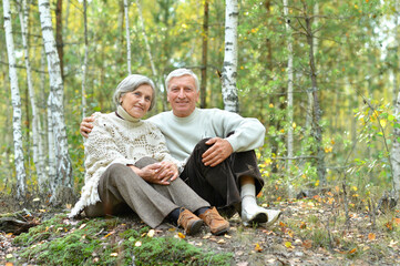 Portrait of happy senior couple sitting on lawn in autumn birch forest