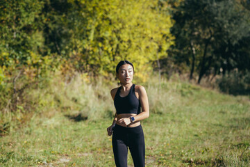 Naklejka na ściany i meble Beautiful Asian woman running in the morning in the park, a woman dressed in a dark sports suit