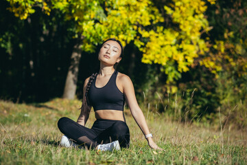 Naklejka na ściany i meble young beautiful sports girl asian woman meditating in park, sitting lotus pose practicing yoga mat, zen. relaxes outdoors in nature in the morning Concept healthy lifestyle, relax, calm, meditation
