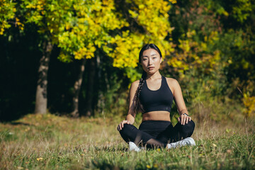 young beautiful sports girl asian woman meditating in park, sitting lotus pose practicing yoga mat, zen. relaxes outdoors in nature in the morning Concept healthy lifestyle, relax, calm, meditation